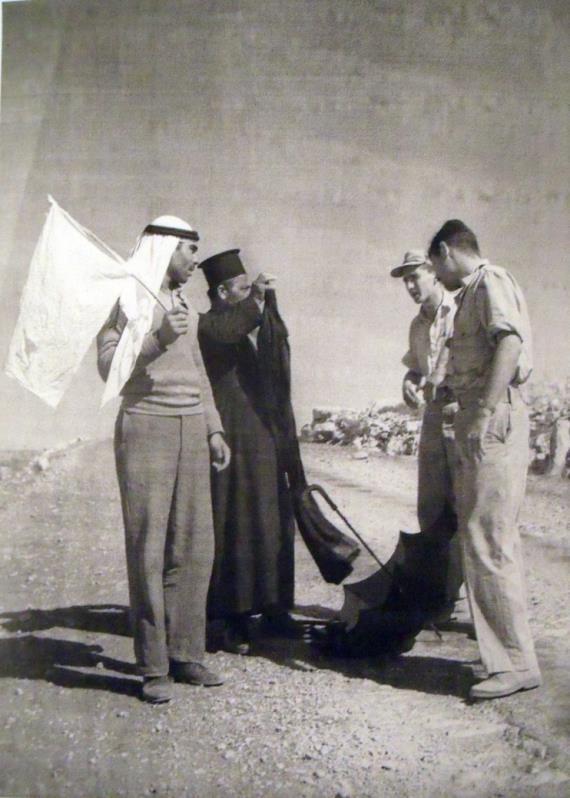כומר קתולי ובן לוויה מציגים דגל כניעה לבן, על יד חיילי
