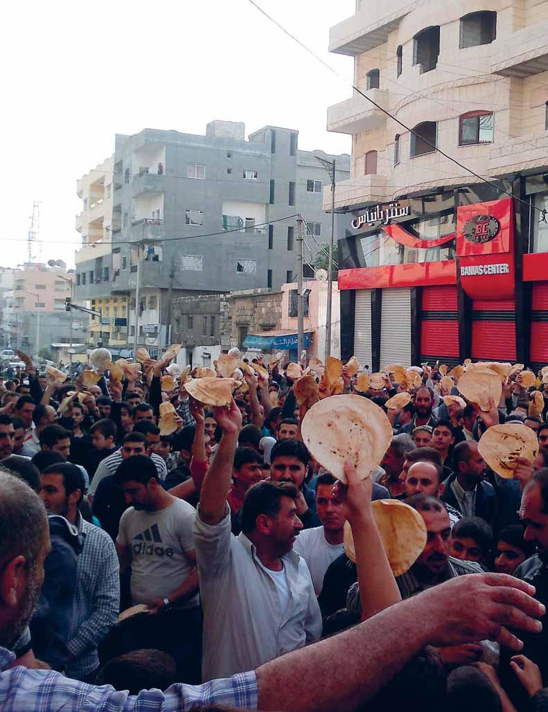 מפגינים עם פיסות לחם צועקים סיסמאות במהלך הפגנה בעיר הסורית בניאס, על